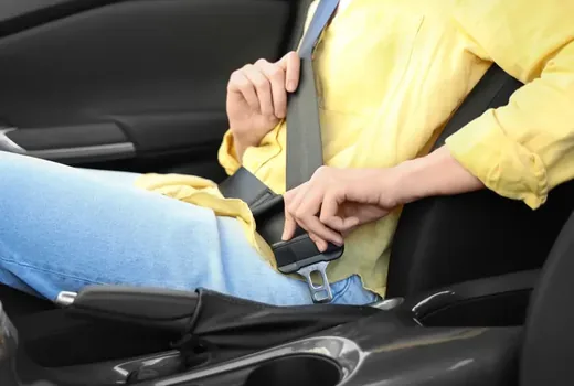 Person fastening a seat belt in a car, with the webbing and buckle clearly visible.