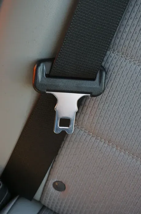 Seat belt webbing and latch plate resting against a grey fabric vehicle seat.