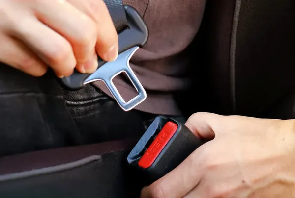 Hands guiding a seat belt latch plate into the buckle receiver.