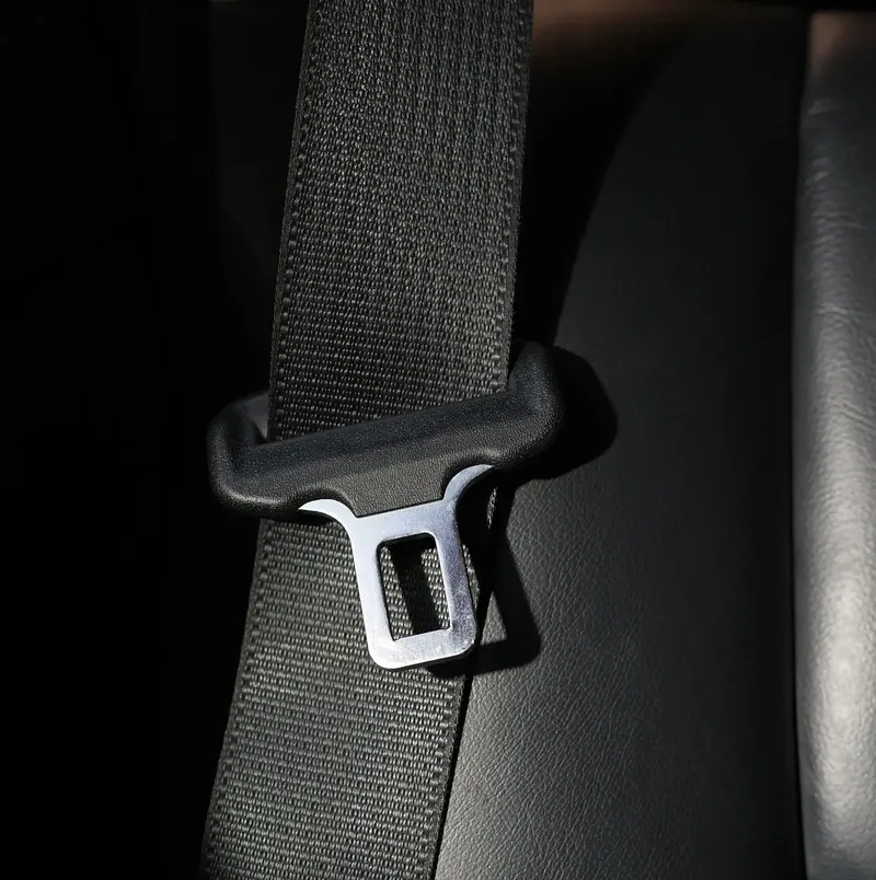 Seat belt webbing threaded through a metal latch plate, photographed close up.