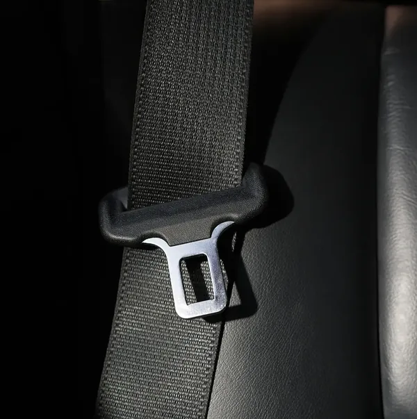 Seat belt webbing running through a metal latch plate inside a dark vehicle interior.