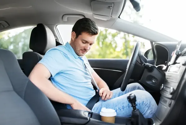 Driver reaching across to draw the seat belt in the front seat of a passenger car.