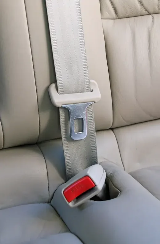 Three-point seat belt fastened on a light-coloured rear seat, shoulder strap and lap section clearly visible.